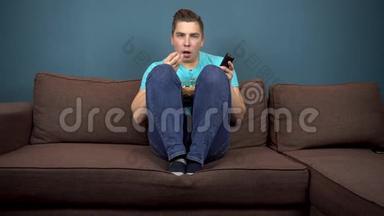 一个年轻人正在看电视和吃爆米花。 那家伙正在仔细看电视。 一个激动人心的时刻